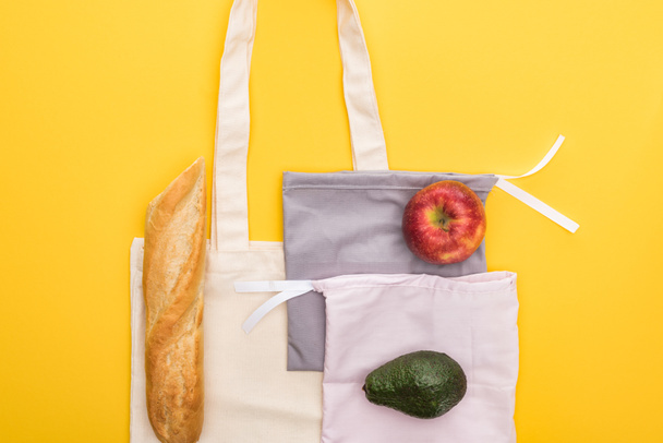 top view of apple, baguette and avocado on eco friendly bags isolated on yellow - Φωτογραφία, εικόνα