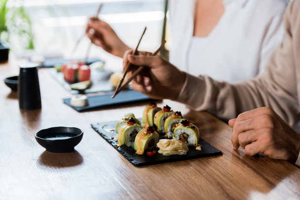 vista recortada del hombre sosteniendo palillos cerca de rollos de sushi y la mujer
  - Foto, Imagen