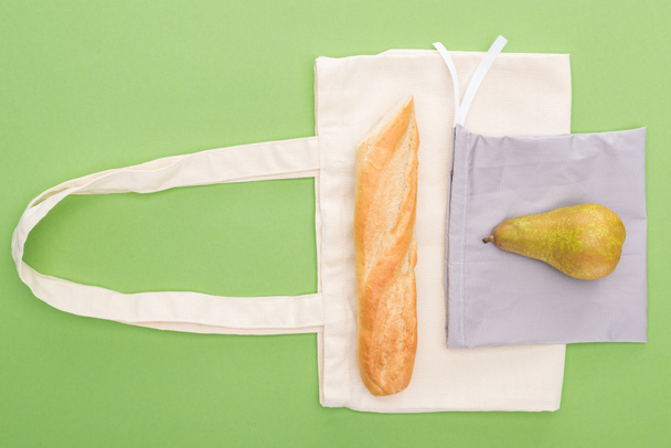top view of pear and baguette on eco friendly bags isolated on green - Fotoğraf, Görsel