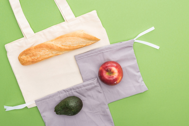 Widok z góry na bagietki, jabłko i awokado na ekologiczne torby izolowane na zielono - Zdjęcie, obraz