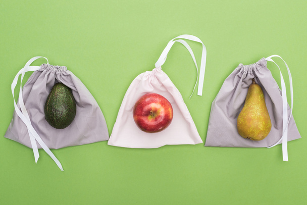 top view of avocado, pear and apple on eco friendly bags isolated on green - Foto, Bild