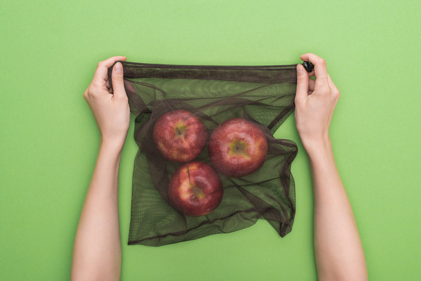 partial view of woman holding red ripe apples in eco friendly bag isolated on green - Fotoğraf, Görsel