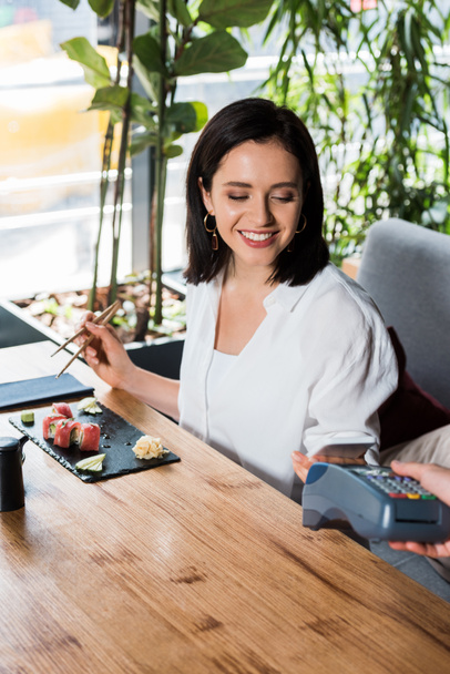 cropped view of waiter holding credit card reader near woman paying with smartphone  - Foto, Bild