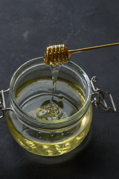 Glass jar full of honey with metal honey dipper on dark rustic background - Photo, Image