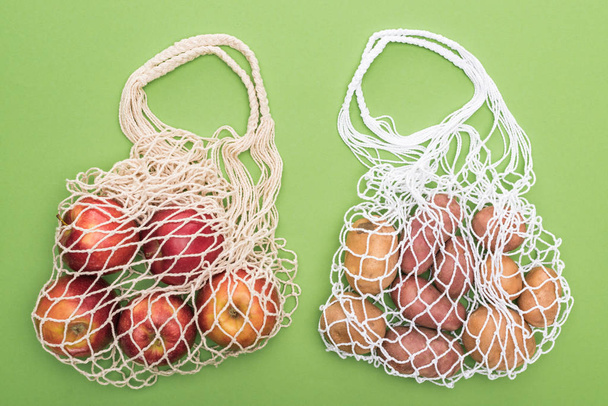 top view of ripe apples and potatoes in string bags isolated on green - Fotoğraf, Görsel