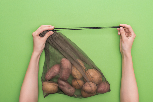 cropped view of woman holding eco friendly bag with potatoes isolated on green - Fotó, kép