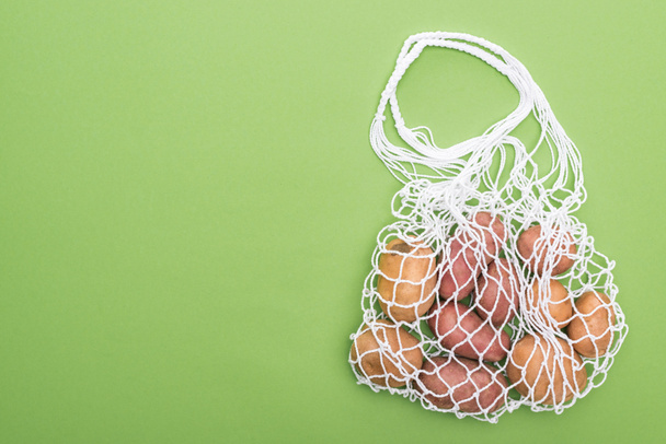 top view of fresh potatoes in eco friendly string bag isolated on green - Foto, imagen