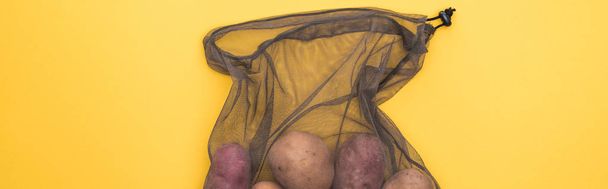 Top zicht van aardappelen in eco vriendelijke Zwarte mesh tas geïsoleerd op geel, panoramische schot - Foto, afbeelding