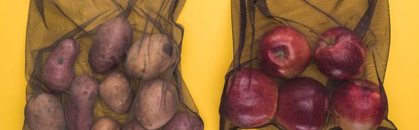 Κορυφαία όψη των γεωμήλων και των μήλων σε φιλικά προς το οικολογικό μαύρο πλέγμα σακούλες απομονώνονται σε κίτρινο, πανοραμική βολή - Φωτογραφία, εικόνα