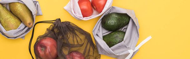 top view of ripe apples, pears, tomatoes, avocado in eco friendly bags isolated on yellow, panoramic shot - Photo, Image