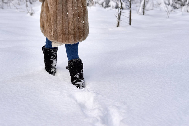 Een vrouw in de winter laarzen loopt door de sneeuw. - Foto, afbeelding