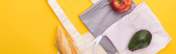 top view of apple, baguette and avocado on eco friendly bags isolated on yellow, panoramic shot - Fotografie, Obrázek