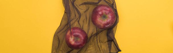 pohled na červená jablka v ekologicky přátelném černém pytli izolovaně na žluté, panoramatické výstřelu - Fotografie, Obrázek