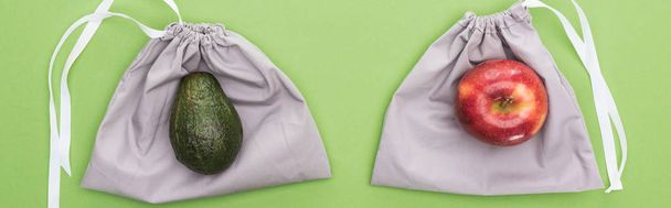 top view of avocado and apple on eco friendly bags isolated on green, panoramic shot - Fotó, kép