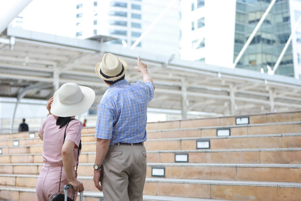 азіатська подруга-мандрівник чоловік і дружина в рожево-блакитній сорочці з білим гарним капелюхом і багажем, що йде в центрі міста, він вказує на щось з правильним місцем для тексту
 - Фото, зображення
