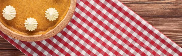 panoramic shot of delicious pumpkin pie with whipped cream on checkered napkin on wooden table - Photo, Image