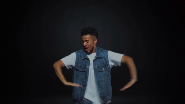 usmívající se africký Američan v džínách tanec na černém  - Záběry, video