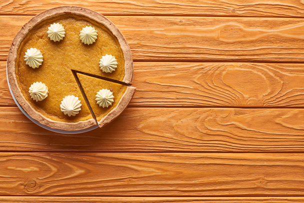 top view of delicious, cut pumpkin pie with whipped cream on orange wooden table - Foto, Bild