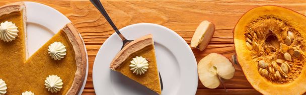 panoramic shot of delicious pumpkin pie with whipped cream near half of raw pumpkin, and cut apple on orange wooden table - Foto, afbeelding