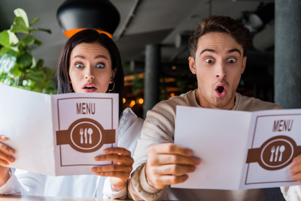 shocked man and woman looking at menus in restaurant  - Фото, изображение