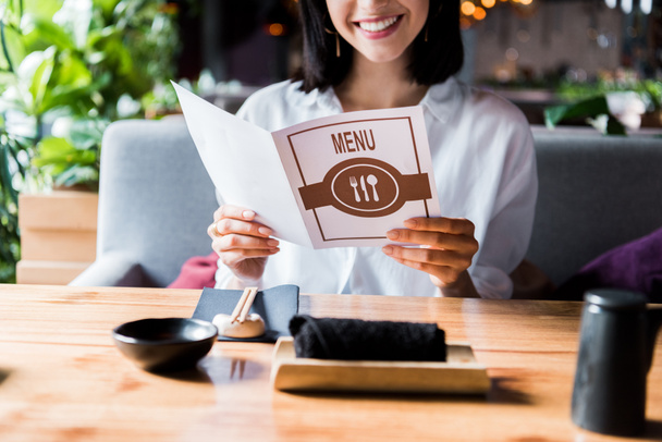 vue recadrée d'une femme joyeuse assise dans un bar à sushi et tenant le menu
  - Photo, image