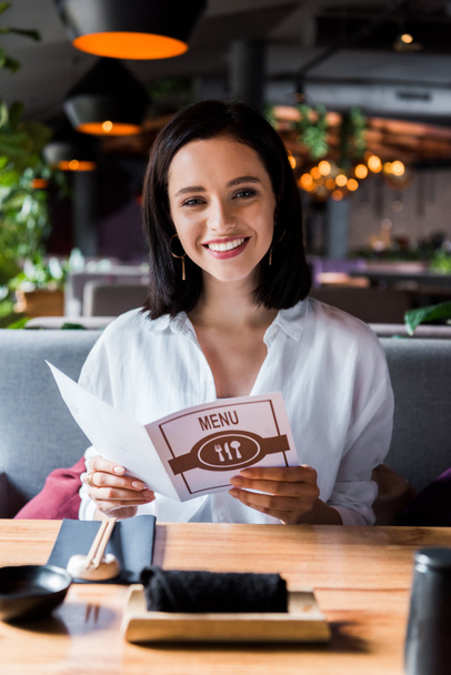 selective focus of cheerful woman sitting in restaurant and holding menu  - Photo, Image