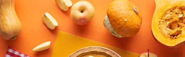 frische, ganze und geschnittene Kürbisse und Äpfel in der Nähe von strukturierten Servietten auf orangefarbener Oberfläche - Foto, Bild