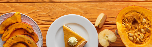 panoramic shot of delicious pumpkin pie with whipped cream near baked and raw pumpkins, and cut apple on orange wooden table - Photo, Image