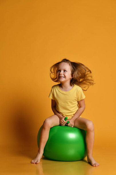 Little sporty girl child in shorts and t-shirt plays jumps on the fit ball. - 写真・画像