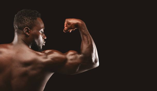 Afro bodybuilder toont sterke biceps op zwarte achtergrond - Foto, afbeelding
