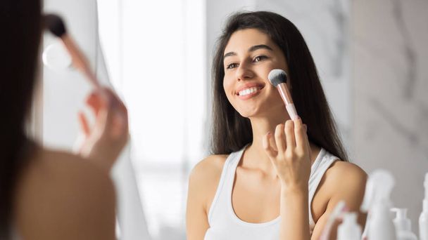Meisje aanbrengen van gezicht poeder met make-up borstel staande in de badkamer - Foto, afbeelding