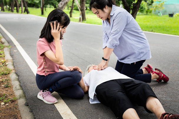 Madre asiática de primeros auxilios de emergencia RCP en la abuela mayor inconsciente, mientras que la hija llama a la ambulancia, la mujer trata de resucitar a la paciente, después de un accidente, ataque al corazón, anciana mujer con paro cardíaco mientras hace ejercicio en el parque
 - Foto, imagen
