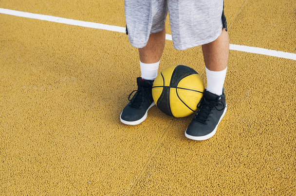 Ноги молодого человека, играющего с мячом на баскетбольной площадке на открытом воздухе
. - Фото, изображение