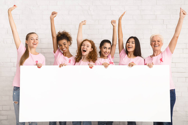 Camisetas de concienciación sobre el cáncer de mama de las señoras que sostienen el tablero en blanco en interiores
 - Foto, imagen