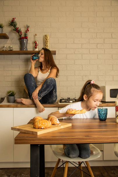 mamá y su hija en la cocina, comer bollos con leche
 - Foto, Imagen