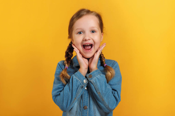 Cheerful emotional little girl on a yellow background. The child is pleased with the good news - Valokuva, kuva