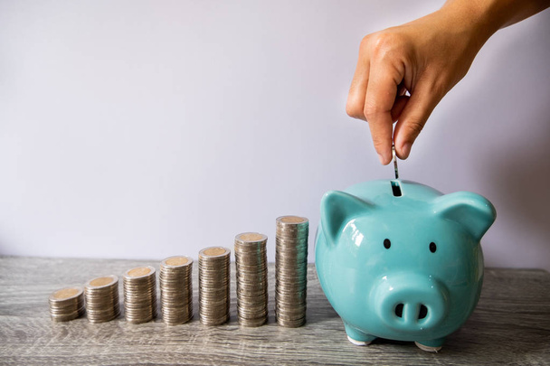 vrouw hand putting Coin in blauwe Piggy Bank met munten groei staafgrafiek, stap omhoog groeiend bedrijf naar succes en besparing voor pensioen concept - Foto, afbeelding