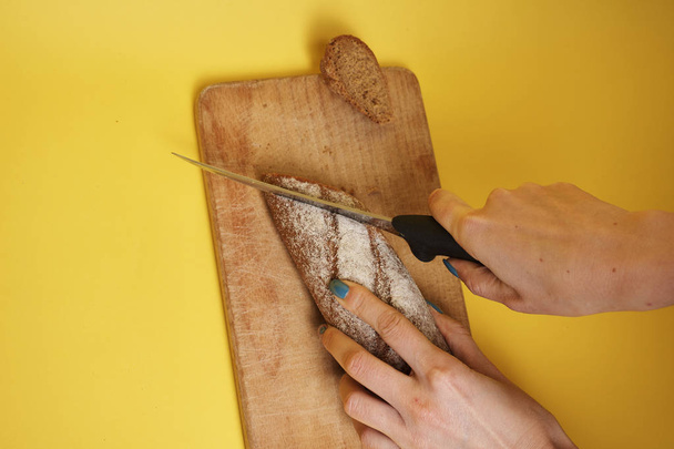 cropped shot of woman holding knife and slicing fresh tasty rye bread   - Foto, Bild