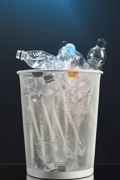 Prullenbak met verspilde plastic flessen, zwarte achtergrond - Foto, afbeelding