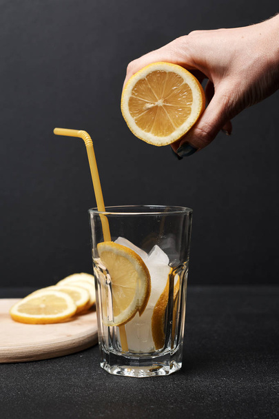 hand holding lemon half over glass with summer fresh cocktail , close view - Zdjęcie, obraz