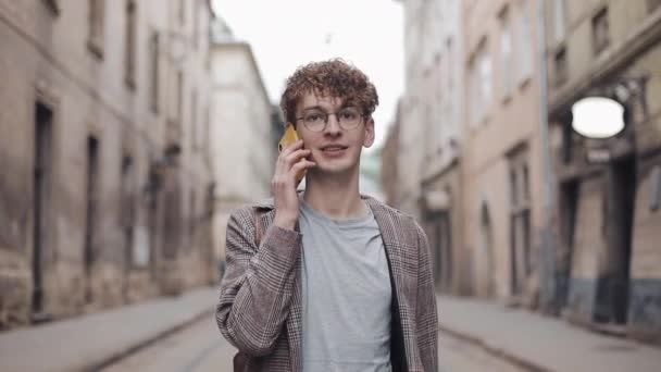 Gözlükgenç Hipster Guy Smartphone Talking Gülümseyen, Onun Watch bakıyor, Blured Old City Arka Plan bir Tarih Yürüyüş sahip. İletişim Kavramı. - Video, Çekim