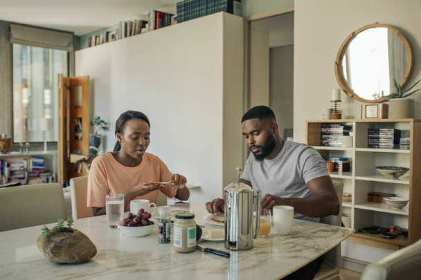 Молодая афроамериканская пара, сидящая вместе за обеденным столом дома, завтракает и пьет кофе по утрам
 - Фото, изображение