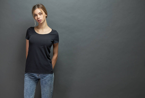 Sexy woman or girl wearing black blank t-shirt with space for your logo, mock up or design in casual urban style over gray background - 写真・画像