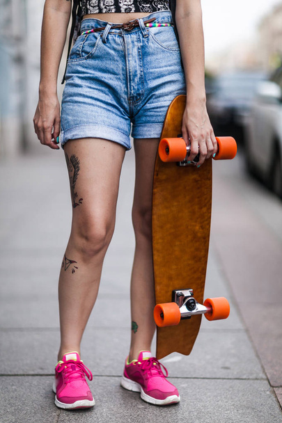 a tattooed girl holds a longboard in her hands - Foto, Imagem