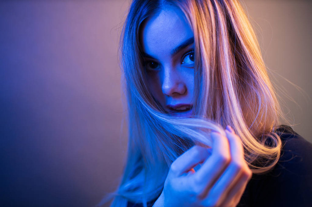 Sexy young blonde girl portrait over gray paper background in neon lights - Fotó, kép