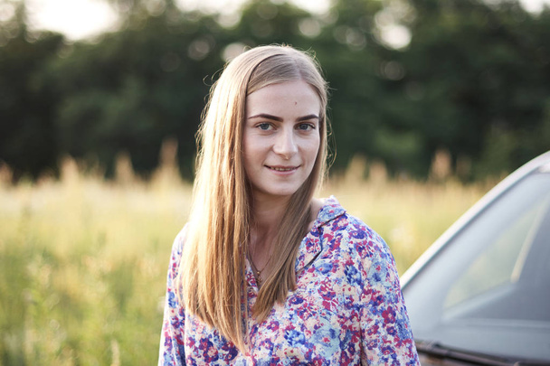 Pretty young woman in dress posing near car on field with flowers - Foto, afbeelding