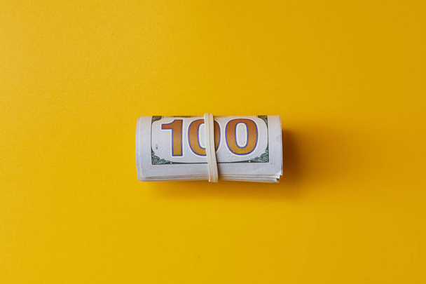 pack of dollars twisted into a roll on yellow background - Fotó, kép