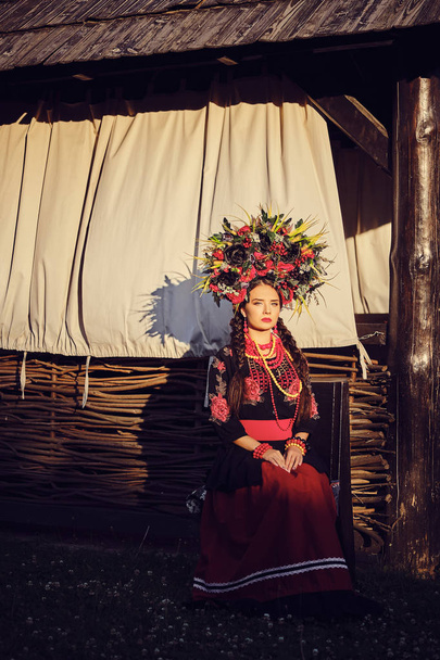 Brunette fille dans un noir et rouge brodé ukrainien costume national authentique et une couronne de fleurs pose contre une terrasse. Gros plan
. - Photo, image