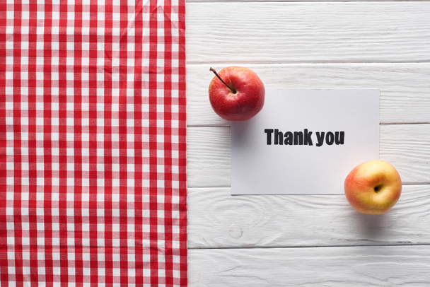 Draufsicht auf reife Äpfel und Dankeskarte auf weißem Holztisch mit karierter Serviette - Foto, Bild