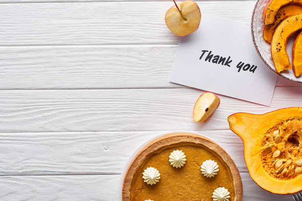 Ansicht von Kürbiskuchen, reifen Äpfeln und Dankeskarte auf weißem Holztisch - Foto, Bild